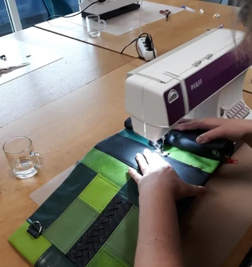 Hand aan de naaimachine die een groene leren tas in elkaar zet